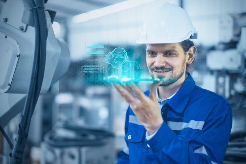 Ingenieur mit Schutzhelm, dem ein Bauteil als Hologramm über der Hand schwebt